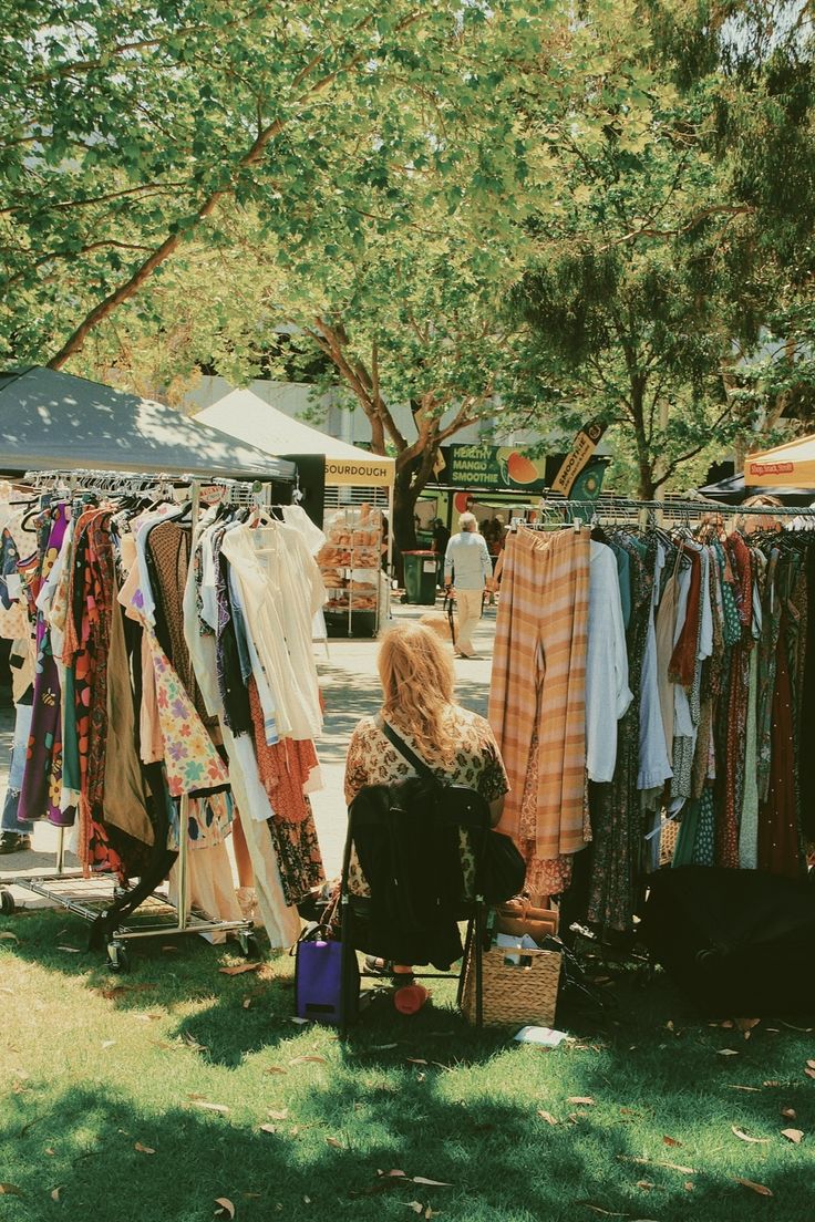 Outdoor market with racks of secondhand clothing under trees